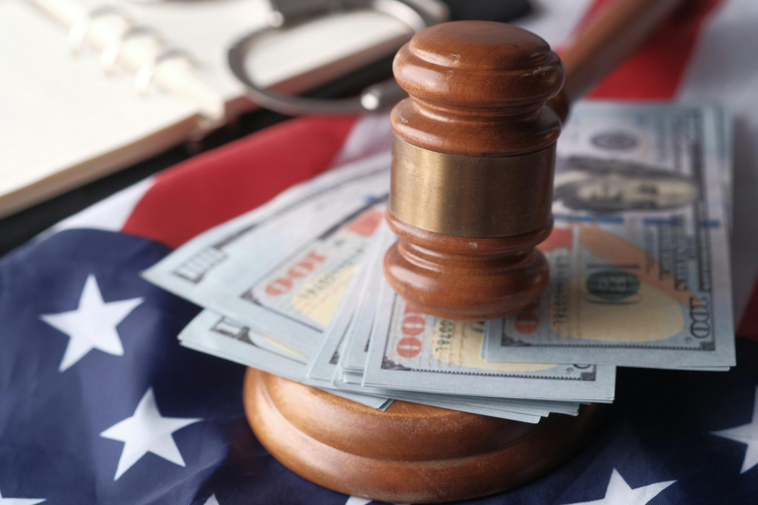 Close-up of a judge's gavel resting on US dollar bills and an American flag, symbolizing justice and finance.